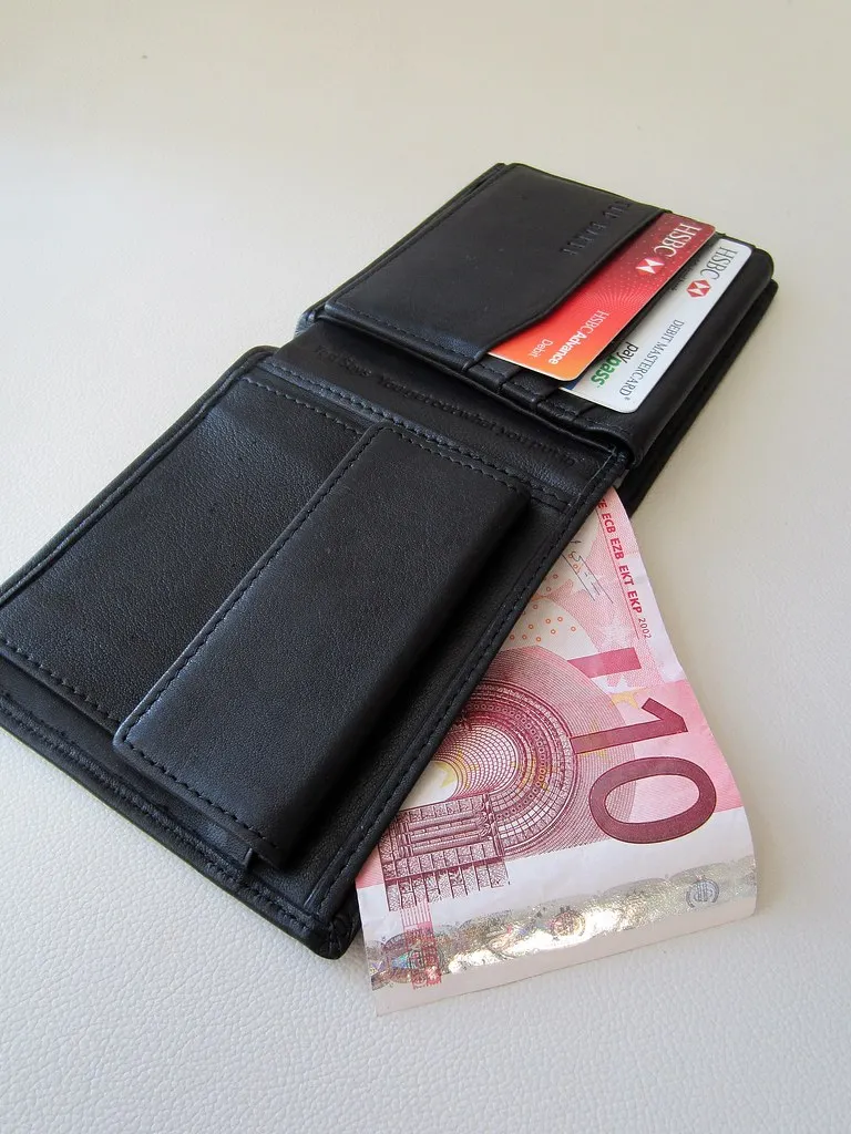 A wallet holding credit cards beside a euro banknote on a light surface